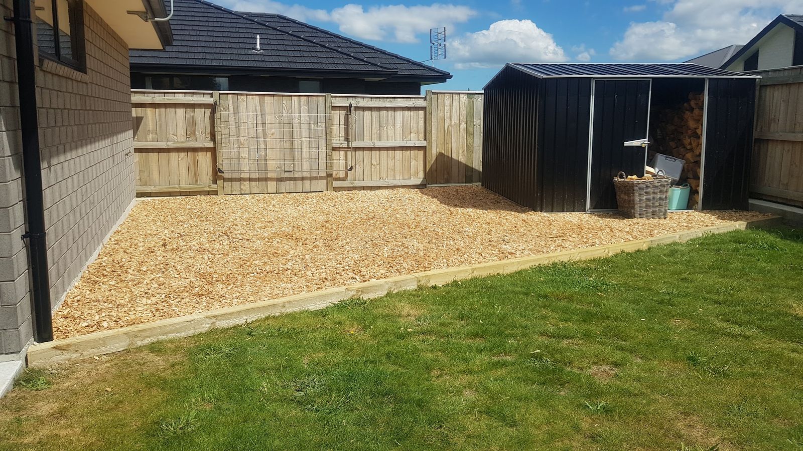 Freshly laid bark-chip area with timber edging beside a shed and lawn